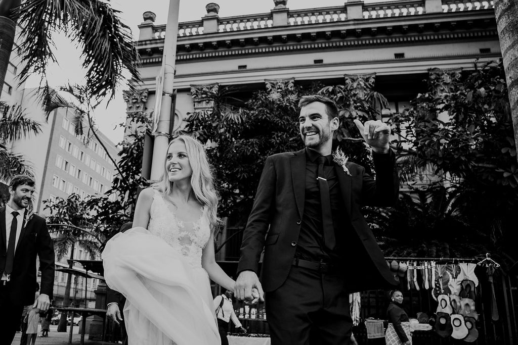 Natural documentary photograph of bride and groom walking happily together through Durban's CBD