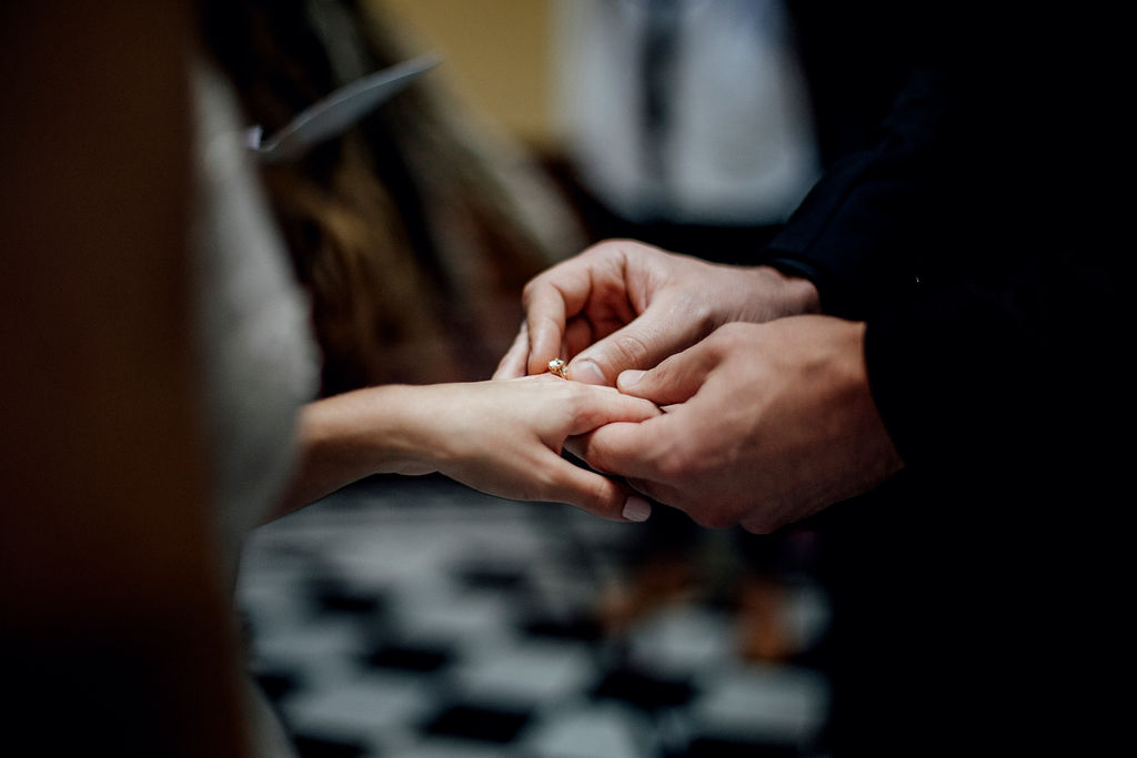 close up image of hands during wedding ceremony whilst groom slip wedding ring onto brides finger