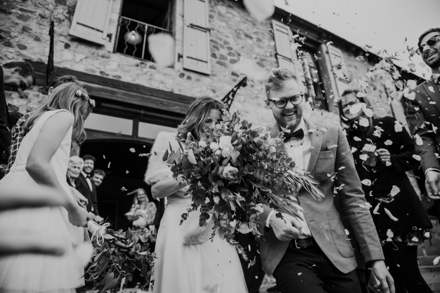 Blurry black and white wedding image of trendy couple emerging from wedding venue whilst being showered with confetti
