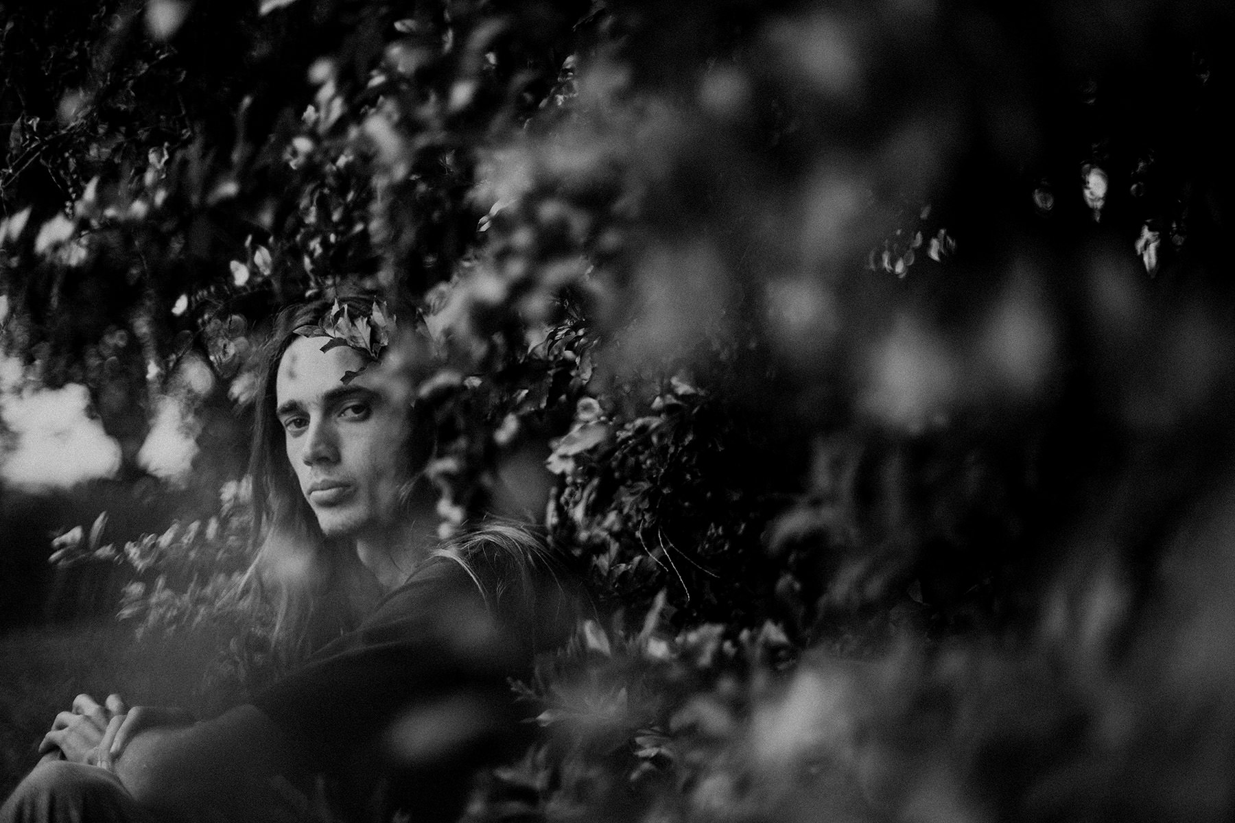 Portrait portfolio image of young man with long hair surrounded by foliage